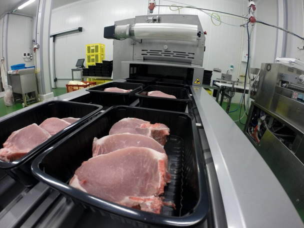 Fresh meat packing machine. Raw sliced pork meat in plastic boxes packaging tray. Meat industry. - Photo, Image