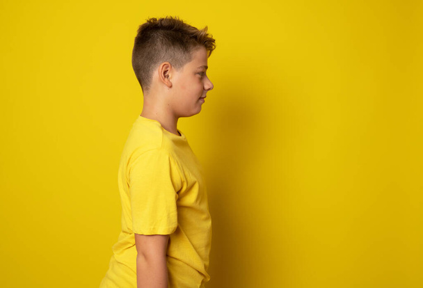 Νεαρό μικρό παιδί φορώντας casual t-shirt στέκεται πάνω από το κίτρινο απομονωμένο φόντο κοιτάζοντας προς τα πλάγια, να χαλαρώσετε προφίλ ποζάρουν με φυσικό πρόσωπο με αυτοπεποίθηση χαμόγελο. - Φωτογραφία, εικόνα