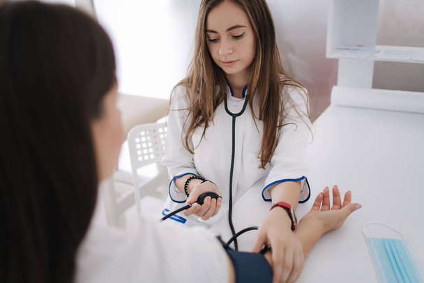 Ženský lékař používající sfygmomanometr se stetoskopem kontrolujícím krevní tlak pacientce v nemocnici. Mladá žena moderní na klinice - Fotografie, Obrázek