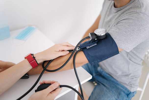 Young man with high blood pressure. Female doctor using sphygmomanometer with stethoscope checking blood pressure to a patient in clinic. Medical exam. Close up - Foto, Imagen
