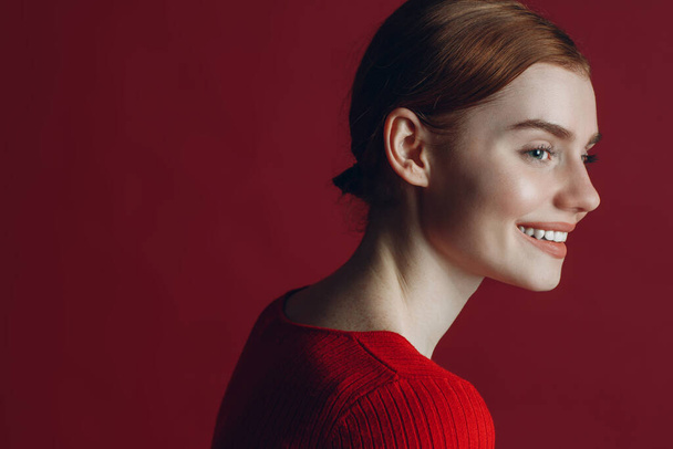 Retrato de joven jengibre sonrisa mujer perfil retrato sobre fondo rojo - Foto, imagen