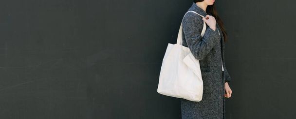 Woman holding white textile tote eco bag in urban area. Ecology or environment protection concept. White eco bag for mock up. - Foto, Bild