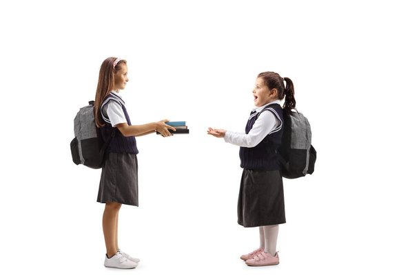 Schoolgirl giving books to a happy girl in a school uniform isolated on white background - Fotó, kép
