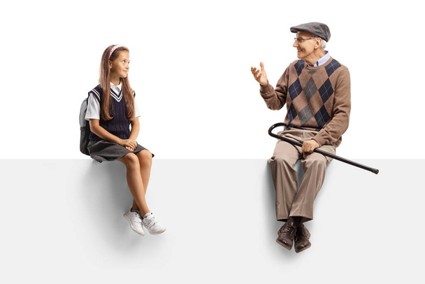 Grandfather and granddaughter sitting on a blank panel and talking isolated on white background - Valokuva, kuva
