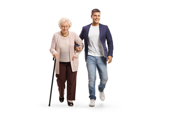 Full length portrait of a young man helping an elderly lady with a walking cane isolated on white background - Photo, image