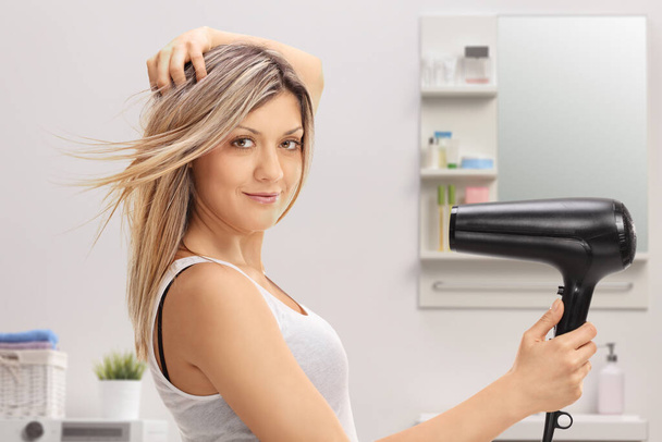 Woman using a hairdryer in a bathroom - Фото, изображение