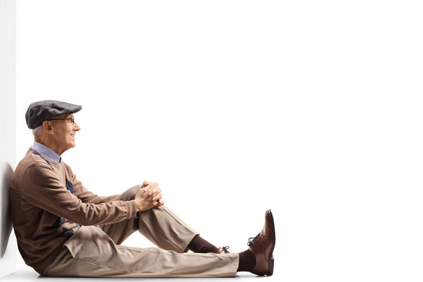 Elderly man sitting on the gorund and leaning on a wall isolated on white background - Photo, Image