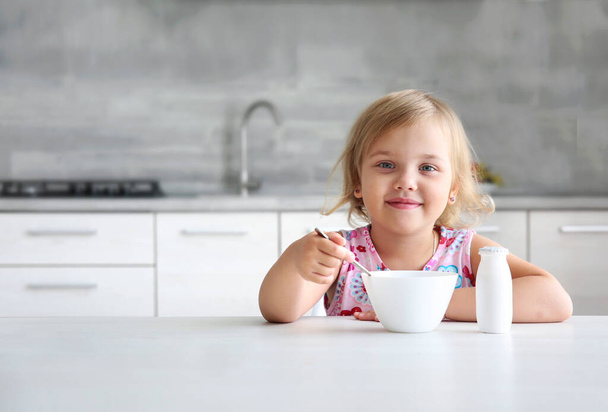Caucasian child sitting at empty space table with bowl and spoon. Advertisement design. Little girl have a meal. Kid eating at kitchen breakfast. - Fotó, kép