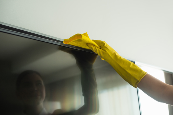 καλλιεργημένη άποψη της οικονόμου σε λαστιχένια γάντι καθαρισμού οθόνη τηλεόρασης με κουρέλι - Φωτογραφία, εικόνα