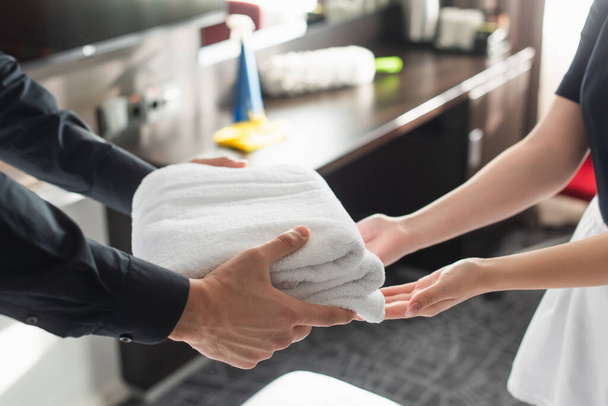 przycięty widok gospodyni dając czyste białe ręczniki pokojówce w pokoju hotelowym  - Zdjęcie, obraz
