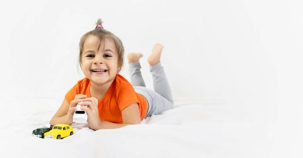 Little girl playing with white toy car. Sitting on the white bedsheet. Smiling. - Zdjęcie, obraz