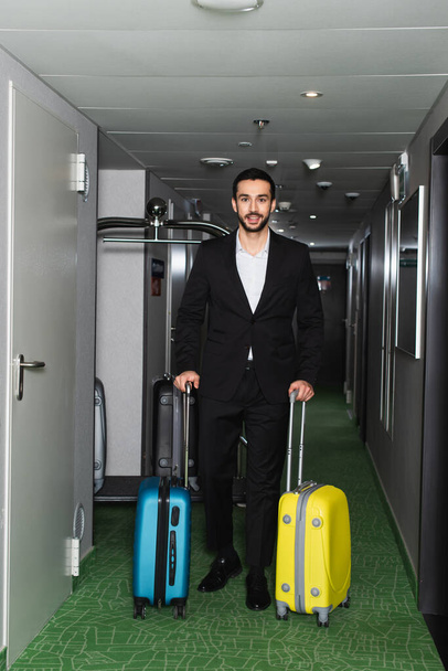 cheerful man walking with baggage in hotel corridor  - Φωτογραφία, εικόνα