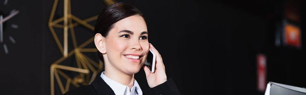 onnellinen vastaanottovirkailija hymyilee ja puhuu älypuhelimella hotellin aulassa, bannerissa - Valokuva, kuva