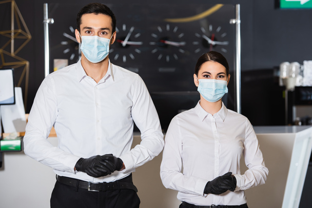 recepcionistas en máscaras médicas y guantes de látex cerca de la recepción - Foto, Imagen