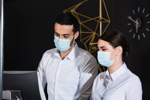 administrátoři v lékařských maskách při pohledu na monitor počítače v recepci  - Fotografie, Obrázek