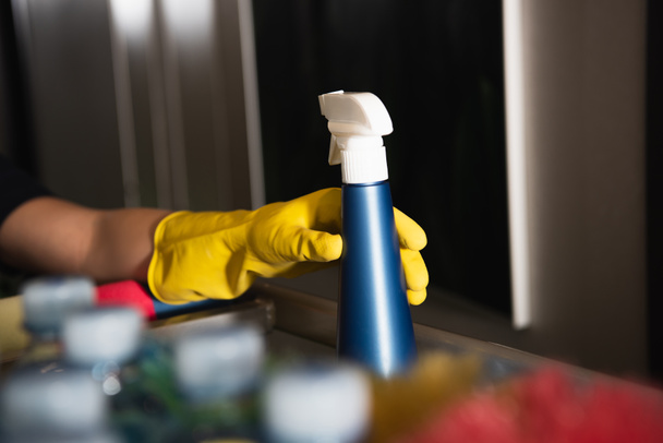 vue recadrée de femme de ménage en gant de caoutchouc atteignant bouteille de pulvérisation  - Photo, image
