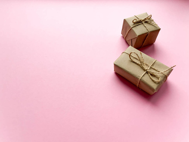 A gift box wrapped in kraft paper on a pink background. View from above, flat lay, top view design. Minimalism. Concept sales, shopping, christmas holidays and birthday. - Фото, изображение