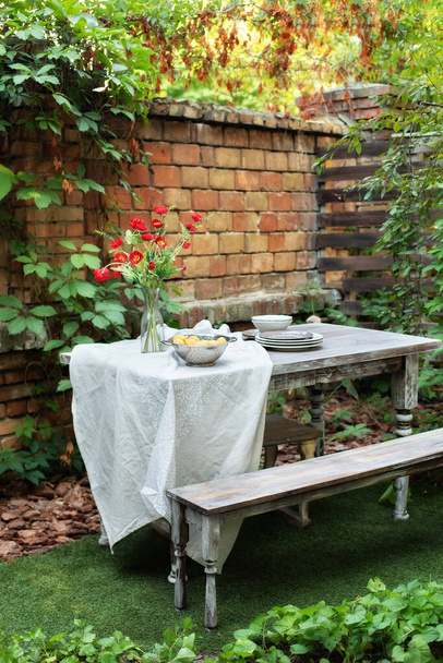 Arka bahçede yemek masası. Avluda ya da balkonda rahat bir yer. Teras evinin önünde tuğla duvar ve bitkilerle, masa ve ahşap bankla. Bahçe yazın veranda, ahşap bahçe mobilyası ve barbekü..  - Fotoğraf, Görsel