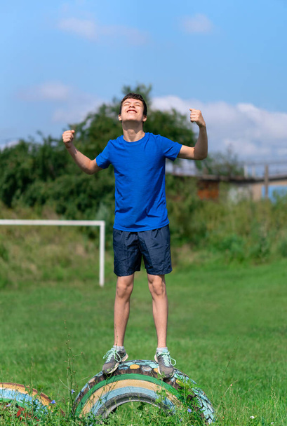 Genç bir çocuk dışarıda spor yapıyor, bahçede spor yapıyor, tekerleğin üzerinde duruyor ve kaslarını gösteriyor, sağlıklı bir yaşam tarzı. - Fotoğraf, Görsel