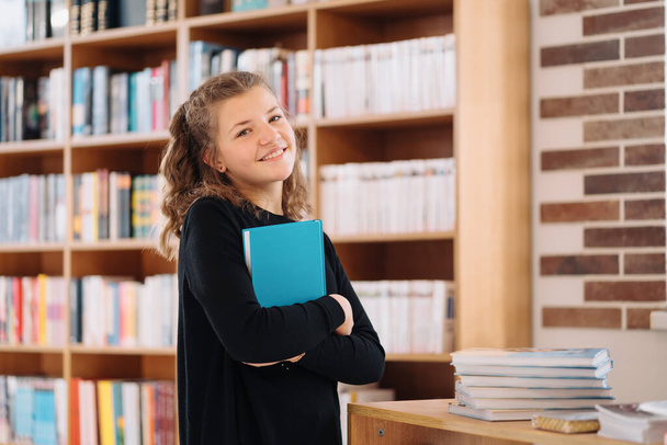 Teenager girl holding a book among many books - Photo, Image