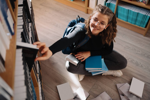 Adolescente chica escogiendo un libro en un estante de la biblioteca - Foto, Imagen