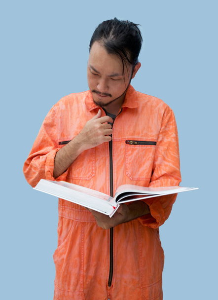 Le chef mécanicien en uniforme orange tenant un gros livre. Tenez-vous debout et lisez attentivement le manuel d'entretien. Portrait avec lumière de studio
. - Photo, image