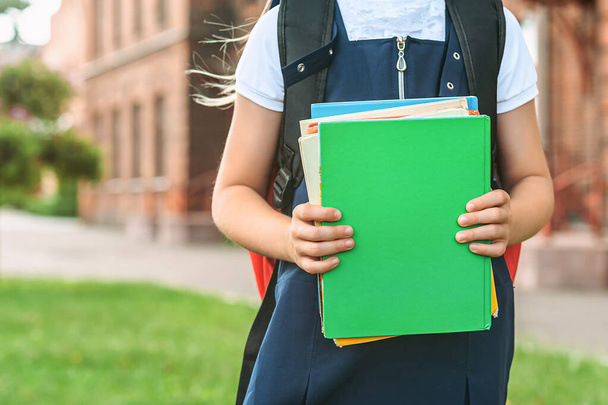 Close-up, A child of an elementary school student holds books in her hands and goes back to school. First day of study. Against the background of the old college. Concept on the topic of education - Foto, imagen