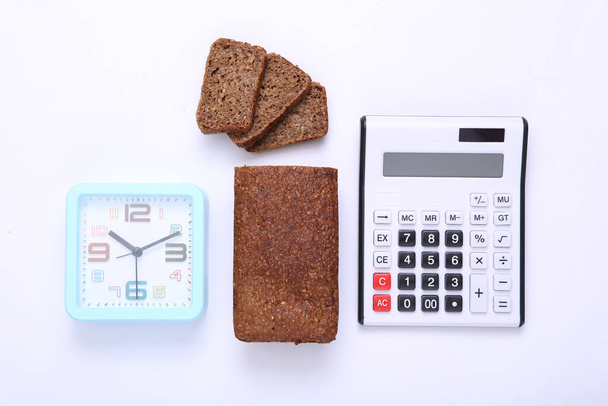 Calculatrice avec horloge, pain de seigle à grains entiers tranché sur fond blanc. Régime alimentaire, concept de comptage des calories - Photo, image
