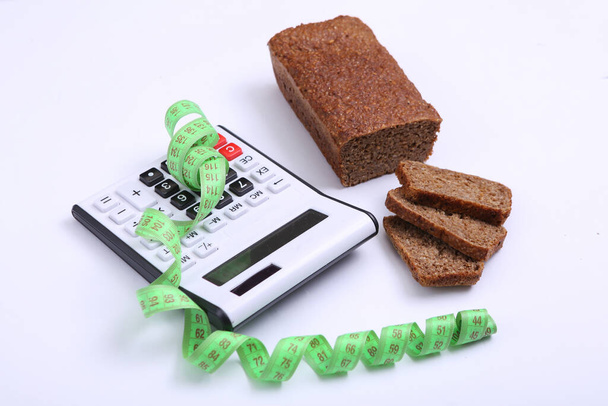 Taschenrechner mit Maßband und Roggenvollkornbrot auf weißem Hintergrund. Ernährung, Kalorienzählung - Foto, Bild