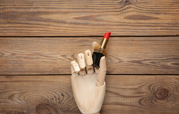 Mão de madeira segura batom no fundo de madeira - Foto, Imagem