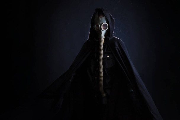 A gloomy man in dark clothes, a black hood on his head, a gas mask protects his face. - Fotoğraf, Görsel