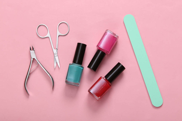 Маникюрные принадлежности. Лак для ногтей бутылки, ножницы и пилка для ногтей на розовом фоне. Вид сверху. Плоский лежал - Фото, изображение