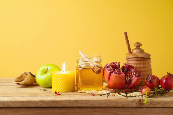 Jewish holiday Rosh Hashana concept with honey jar, apple and pomegranate on wooden table over yellow background - Fotó, kép