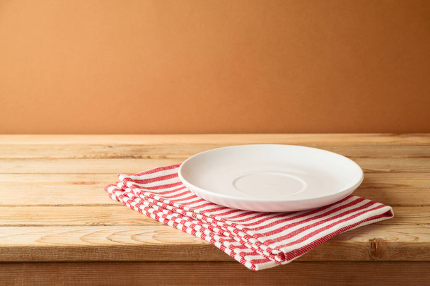 Empty white plate on wooden table with tablecloth.  Kitchen mock up for design and product display. - Фото, зображення