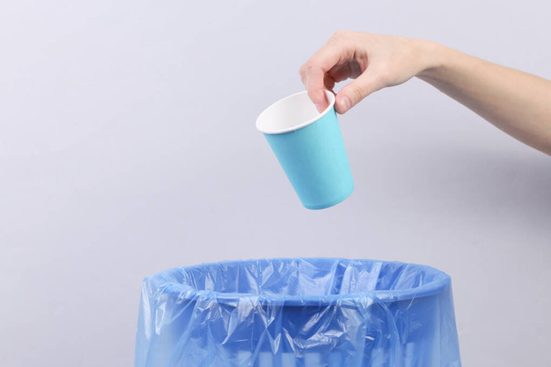 Hand throws paper cup into trash bin with package on gray background - Photo, Image