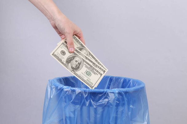 Hand throws dollar bills into trash bin with package on gray background - Fotoğraf, Görsel