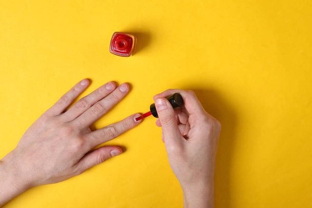 Weibliche Hände lackieren Nägel mit rotem Nagellack auf gelbem Hintergrund - Foto, Bild