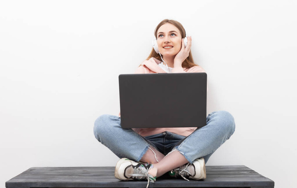 Vidám kaukázusi nő zenét hallgat fejhallgatóval és laptopot használ fehér alapon - Fotó, kép