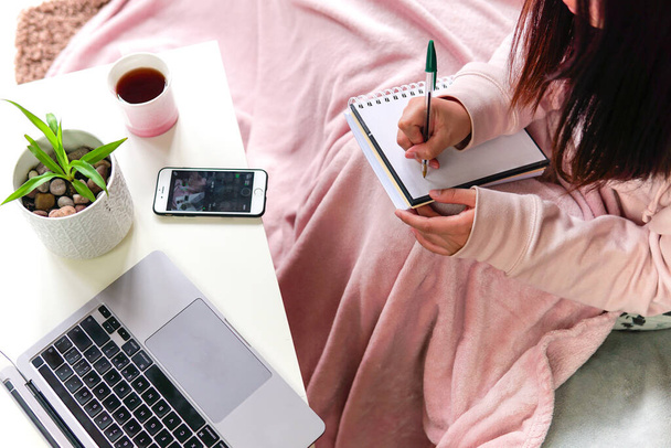 Nő borító rózsaszín takaró ül kanapén jegyzetel notebook laptop az asztalon. otthon tanulás vagy munka. - Fotó, kép
