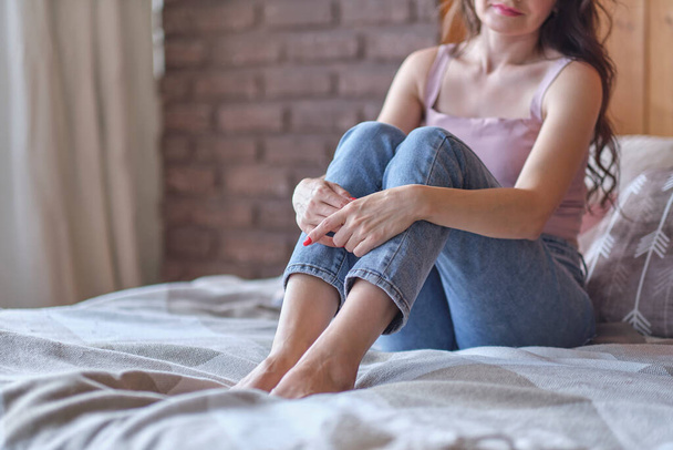 nepoznatelné ženy, které si oblékají džíny a objímají si kolena na posteli. deprese, koncepce osamělosti - Fotografie, Obrázek