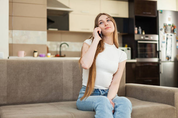 Bonito jovem mulher falando ao telefone enquanto sentado no sofá na sala de estar - Foto, Imagem
