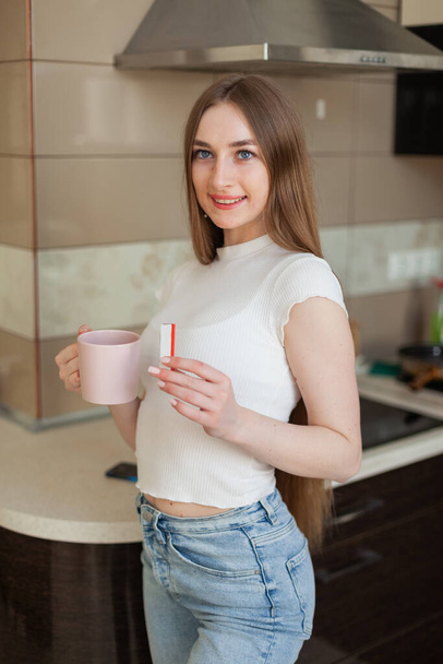 Young cheerful woman drinking coffee and eating chocolate bar in the kitchen - Foto, Bild