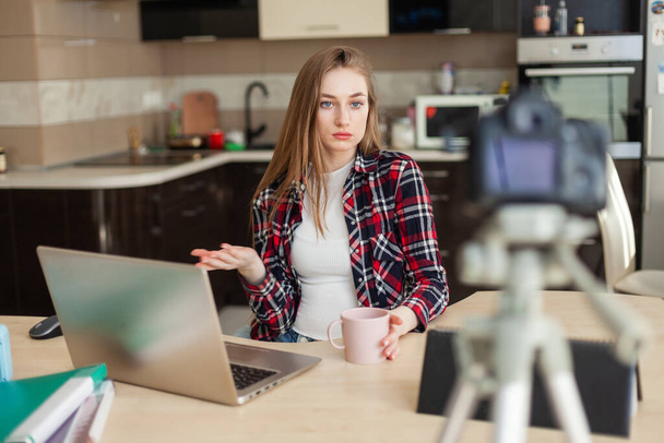 Kadın blogcu, dizüstü bilgisayarla masada otururken blogunu kameraya kaydediyor - Fotoğraf, Görsel