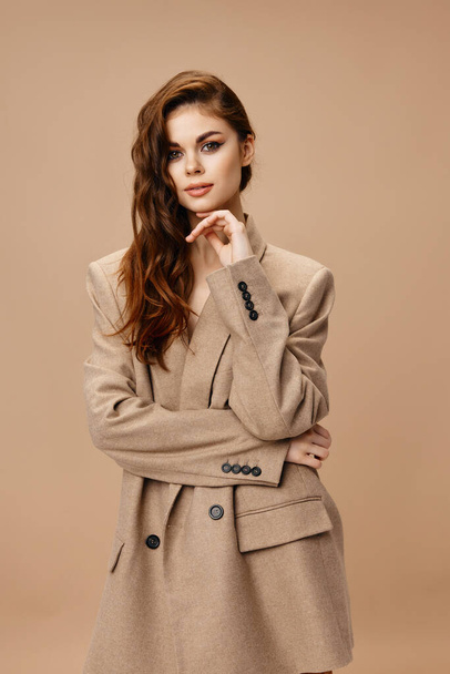 donna attraente in cappotto beige tocca il viso con mano e acconciatura e trucco - Foto, immagini