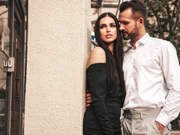 Beautiful fashion woman and her handsome elegant boyfriend in suit. Sexy brunette model in black evening dress. Fashionable couple posing in the street in Europe. Brutal man and his female outdoors - Foto, Imagen
