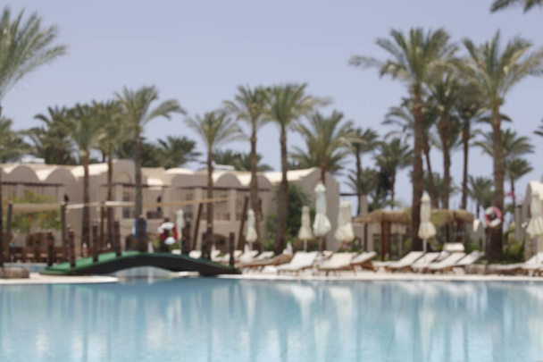 Egipto, Sharm el-Sheik, 06.01.2021, vista de la zona de la piscina con tumbonas y palmeras dentro del hotel en desenfoque. vacaciones de verano. naturaleza fondo - Foto, imagen