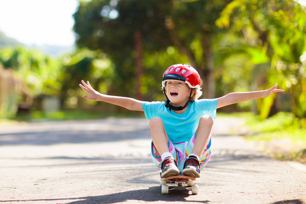 Kid with skateboard. Child riding skate board. Healthy sport and outdoor activity for school kids in summer. Sports fun. Helmet for safe exercise. Boy skater in sunny park. Children training. - Φωτογραφία, εικόνα