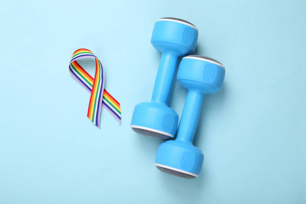 Символ гордости ЛГБТ-радуги и гантели на синем фоне. Концепция спорта и любви. Вид сверху. Плоский лежал - Фото, изображение