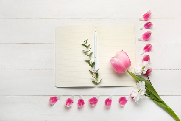 Composição com caderno aberto, caneta e flores sobre fundo de madeira clara - Foto, Imagem