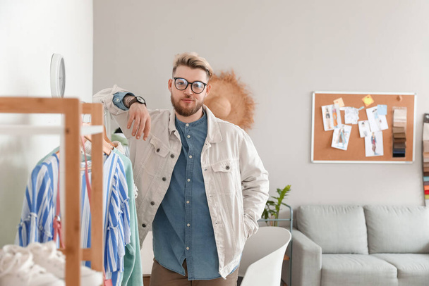 Estilista masculino cerca de rack con ropa en estudio - Foto, Imagen